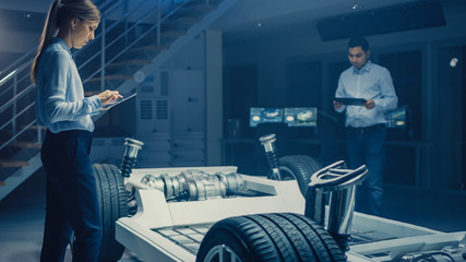 Fototapete - Team of Automotive Engineers Working on Electric Car Chassis Platform, Taking Measures, working with 3D CAD Software, Analysing Efficiency. Vehicle Frame with Wheels, Engine and Battery