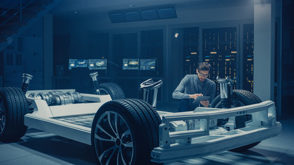 Fototapete - Automobile Engineer Working on Electric Car Platform Chassis Prototype, Using Tablet Computer with 3D CAD Software Modelling. Innovative Facility: Vehicle Frame with Engine, Battery and Suspension