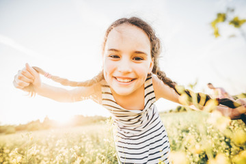 A little girl with two pigtails looking to the camera and smiling in a rapeseed field at the sunset. Concept of happy summer.