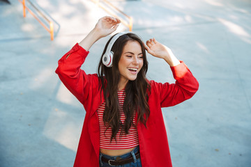 Sticker - Image of happy girl student listening to music with headphones and dancing on sports ground