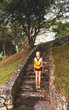 © Artem Markin - Blonde in denim shorts standing in the park on the stone steps. Wearing white jersey, orange backpack. Hands with tattoos. Asia travel