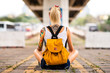 © Artem Markin - Modern girl sits with his back to the camera on a road marking. Carries a yellow backpack, arms tattooed