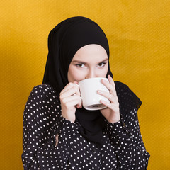 Wall Mural - Pretty arabian woman drinking beverage in cup against surface