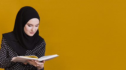 Wall Mural - Islamic woman with headscarf reading book in front of background with copy space