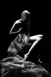 Beautiful young slim busty and leggy naked blonde model girl, sensually covering her nudity with a burlap cloth. Dark background. Conceptual artistic black and white photo