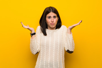 Wall Mural - Young woman over isolated yellow wall having doubts while raising hands