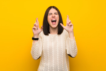 Wall Mural - Young woman over isolated yellow wall with fingers crossing