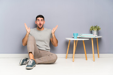 Young handsome man sitting on the floor with surprise facial expression