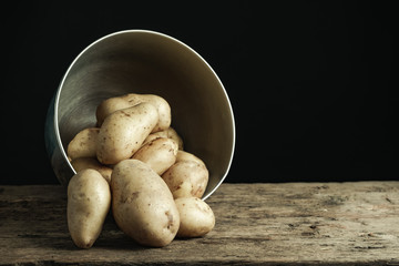 Fresh potato in silver bowl on a old oak wooden table and beautiful black background.