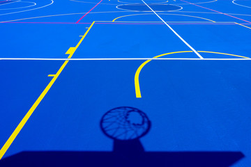 Shadow of a basketball basket on the floor of the court, painted blue and background with lines.