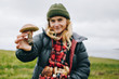 © BublikHaus - Young beautiful woman in camping outdoor outfit for cold harsh weather holds out wild fresh picked mushroom to camera. Concept healthy eating and local organic produce farm