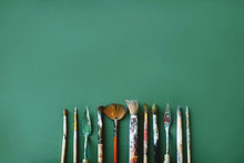 Top View Of Different Sizes Of Brushes And Palette Knife On A Green Background. Art Concept. Space For Text