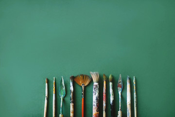 Top view of different sizes of brushes and palette knife on a green background. Art concept. Space for text