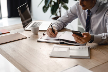 Wall Mural - Businessman writing in daily planner and using smartphone