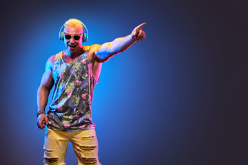 Fashion Muscular DJ man listen to music in colorful neon light with hand up. Handsome blonde Hipster guy Having Fun happy. Art neon fashionable style. Music festival nightclub, summer party concept