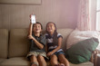 © Cavan for Adobe - Friends (8-9) with smart phone sitting on sofa