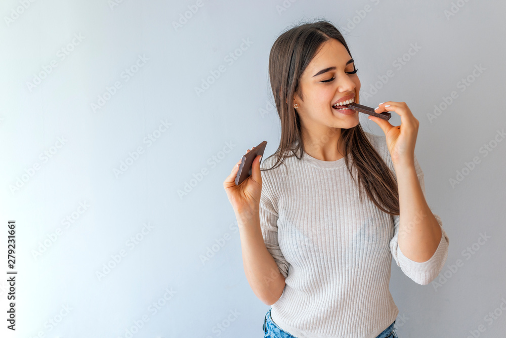 Portrait of a young beautiful girl with dark hair, holding a chocolate bar to enjoy the taste and are dieting, healthy eating and organic foods, feeling temptation.  - obrazy, fototapety, plakaty 