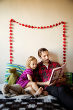 Father And Daughter Reading Book On Bed