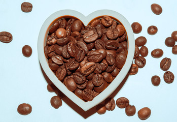 Grains of freshly roasted coffee closeup. Coffee beans are laid out in the shape of a heart. Cup of coffee with beans on white background.