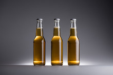 Three Glass Bottles With Beer In Row On Grey Background