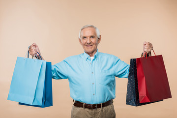 Wall Mural - cheerful senior man smiling while holding shopping bags isolated on beige