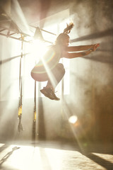 Wall Mural - Higher and higher. Side view of young athletic woman in sport clothing jumping while exercising in professional gym.