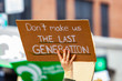 Ecological activists march for change. A cardboard sign is seen closeup in the hand of an environmental campaigner, saying don't make us the last generation, during a rally on an urban city street.
