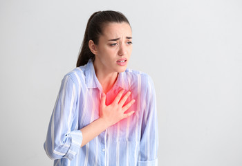 Wall Mural - Young woman suffering from heart attack on light background