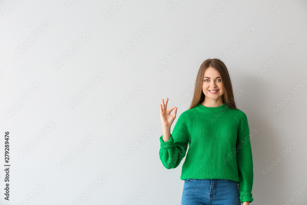 Young deaf mute woman using sign language on light background