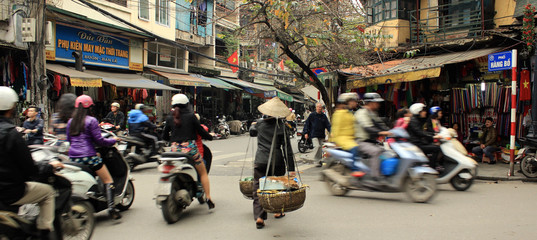 Busy, bustling street intersection in Vietnam, with lots of traffic that includes people walking on foot, and commuting on bikes and scooters on the street