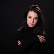 Beautiful girl with dark hair posing over black background. Young pretty woman in studio.