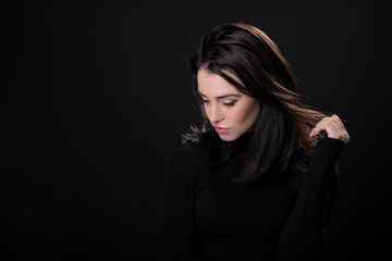 Beautiful girl with dark hair posing over black background. Young pretty woman in studio.