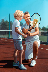 Wall Mural - Curly blonde-haired boy wearing white t-shirt looking at tennis ball