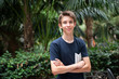 Young boy posing in summer park with palm trees. Cute spectacled smiling happy teen boy 13 years old, looking at camera. Kid's outdoor portrait.