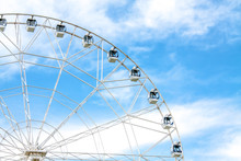 View Of A Part Of A White Ferris Wheel Against A Blue Sky With Snow-white Clouds In An Amusement Park.