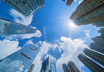 Looking up at modern office buildings. Financial district and business centers in smart city for technology background. Skyscraper and high-rise buildings in Hong Kong at noon with blue sky.