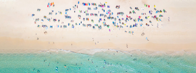 Aerial view crowded public beach with colourful umbrellas, Aerial view of sandy beach with tourists swimming in beautiful clear sea water.