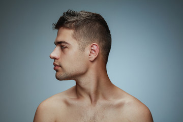 Portrait of shirtless young man isolated on grey studio background. Caucasian healthy male model looking at side and posing. Concept of men's health and beauty, self-care, body and skin care.