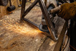 Metalworker uses disc grinder on steel. A closeup view of hot sparks flying from the abrasive disc of an angle grinder whilst a blacksmith polishes a metal frame.