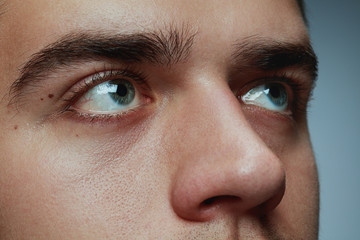 Close-up portrait of young man isolated on grey studio background. Caucasian male model's face and blue eyes. Concept of men's health and beauty, self-care, body and skin care, phycology. Looks calm.