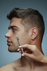 Wall Mural - Close-up profile portrait of young man isolated on grey studio background. Filling botox surgery procedure. Concept of men's health and beauty, cosmetology, self-care, body and skin care. Anti-aging.