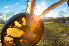 Shaman Holds Sacred Objects Outdoors. A Close Up And Backlit View Of A Native American Drum And Two Eagle Feathers In The Hand Of A Man During Sunset. Sacred Objects Symbolize Wisdom And Virtue.