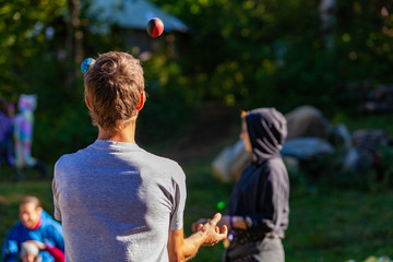 Wall Mural - Fusion of cultural & modern music event. A rear view of a young Caucasian man, juggling balls as young people gather outside tents in the background, during a celebration of traditional cultures.