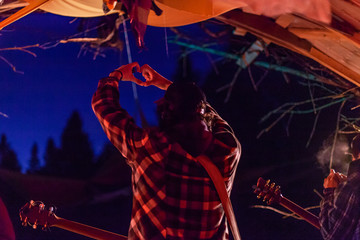 Wall Mural - Fusion of cultural & modern music event. A musician is seen on stage giving the love symbol hand gesture to audience, he has a guitar over shoulder and is viewed from behind by night