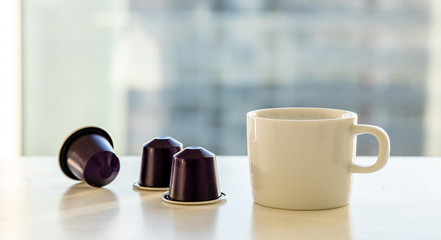 Espresso coffee cup and coffee capsules on a white table. Blur window background