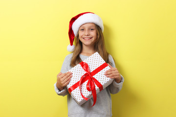 Wall Mural - cute cheerful girl in a Christmas hat on a colored background holding a gift