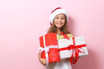 Wall Mural - cute cheerful girl in a Christmas hat on a colored background holding gifts in her hands