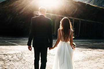 Wall Mural - Unrecognizable married couple walking holding hands against sunset from back.