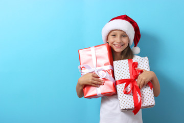 Wall Mural - cute cheerful girl in a Christmas hat on a colored background holding gifts in her hands