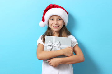 Wall Mural - cute cheerful girl in a Christmas hat on a colored background holding a gift